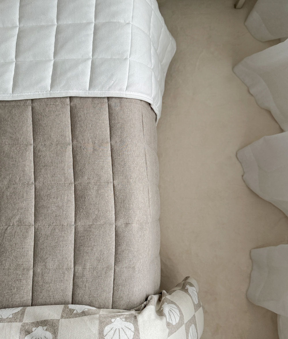 Dune quilt hanging over the end of a bed with an ivory quilt folded above it