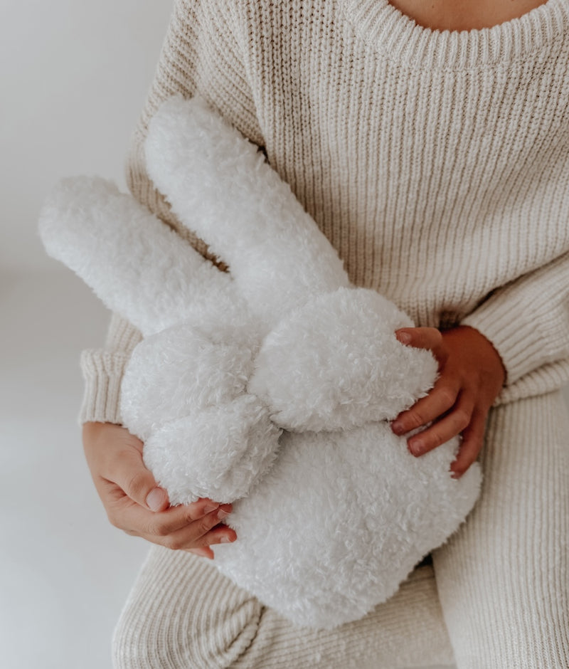 Child in a cream knit holding the Peace Sherpa kids cushion, an ivory peace-sign hand shape