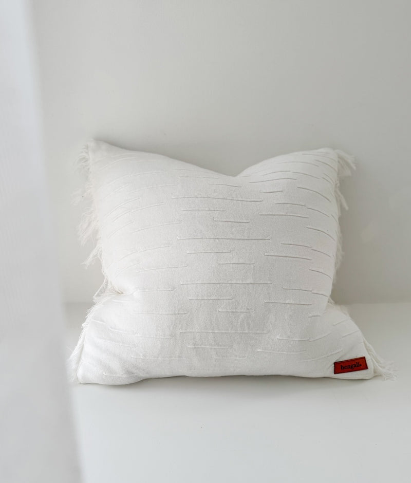 Ivory Flurry cushion cover with raised textured dashes and fringed sides on a white ledge