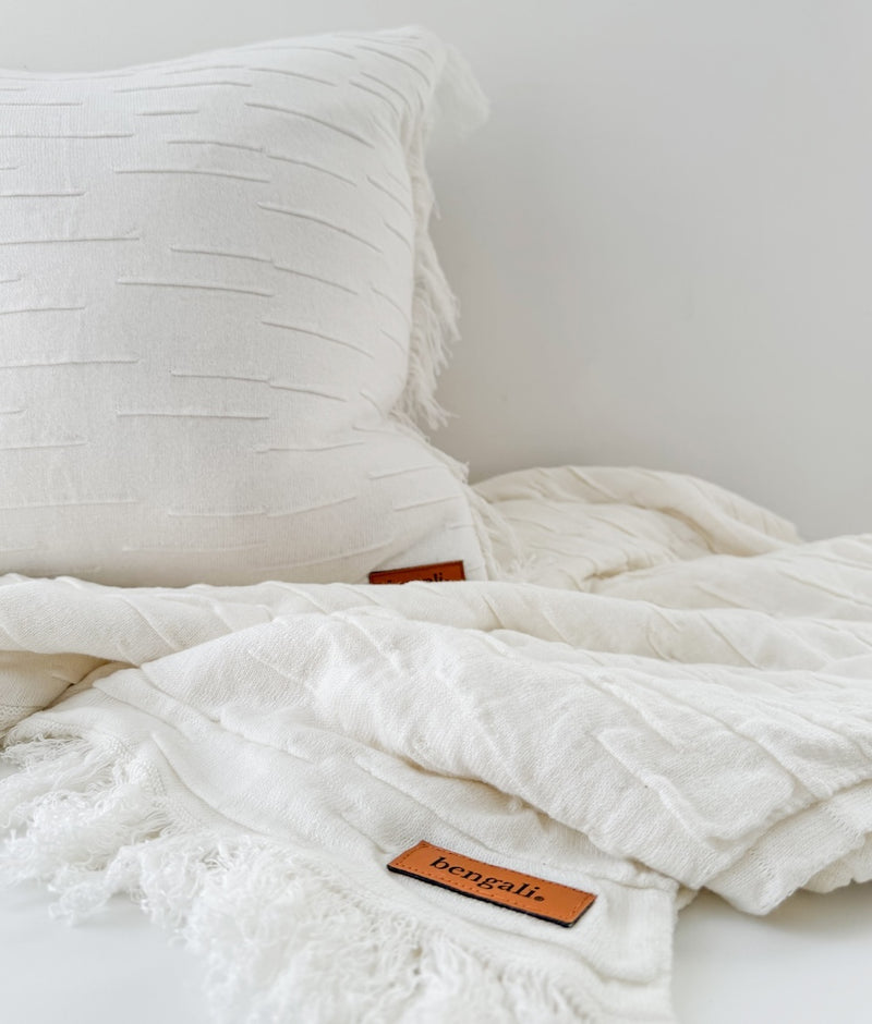 Ivory Flurry cushion cover resting on a fringed ivory throw, both with leather Bengali labels