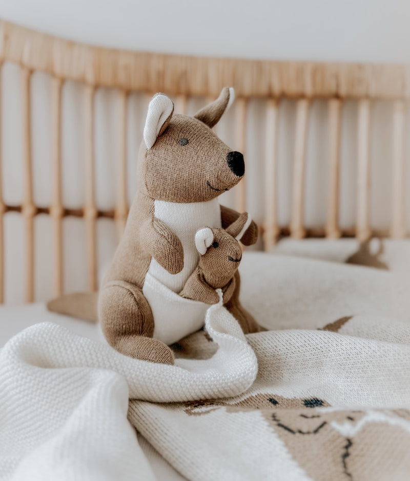 Kangaroo baby comforter snuggly sitting on a Kangaroo knitted blanket in a rattan bassinet
