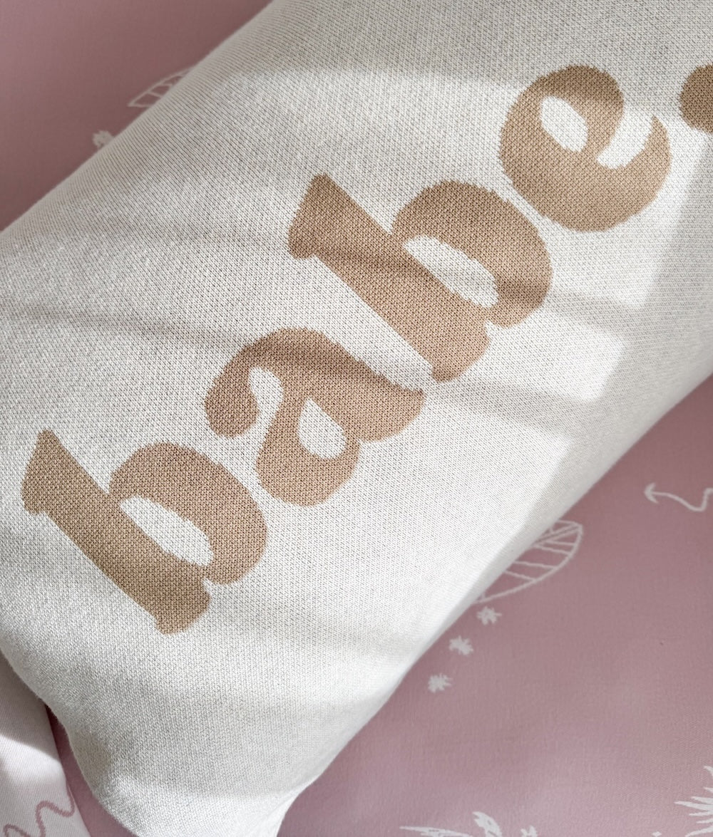 Close-up of the khaki Babe lettering knitted into the natural marle pillowcase