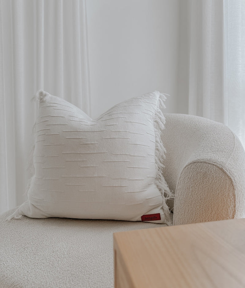 Ivory Flurry cushion cover on a boucle armchair by sheer curtains and a timber side table