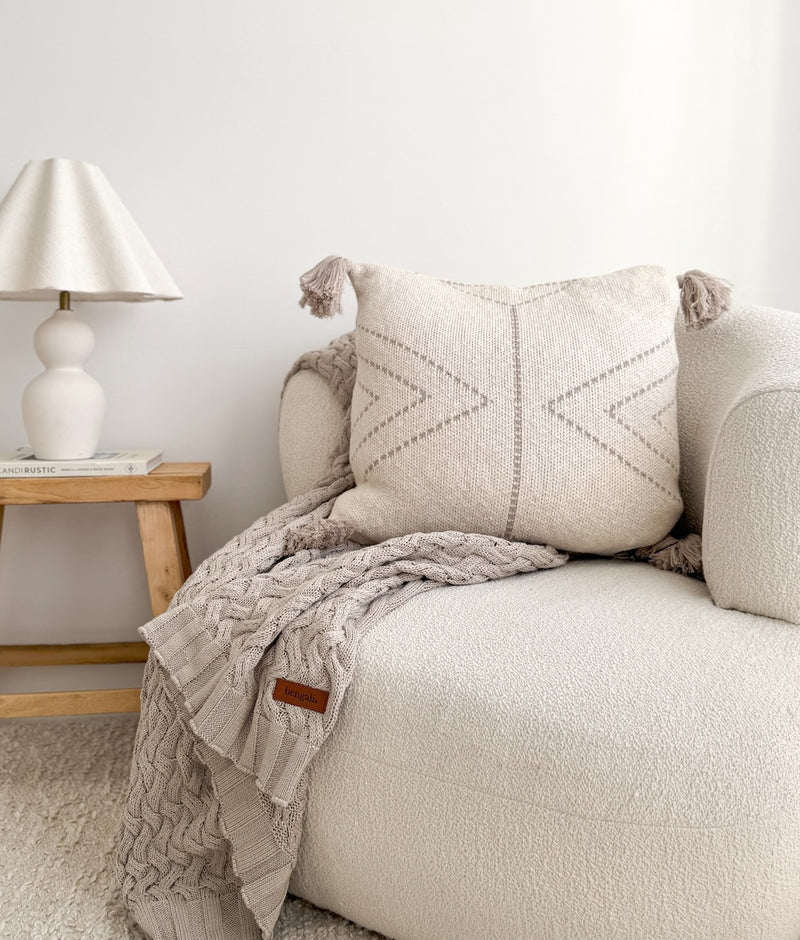 Greige Wave Lounge Throw draped over a boucle sofa beside a tasselled cushion and ceramic lamp