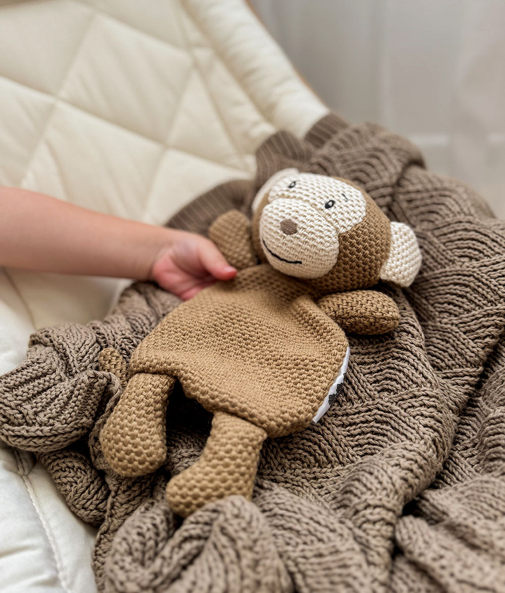 Knitted monkey comforter resting on the stone shell stitch blanket in a bassinet