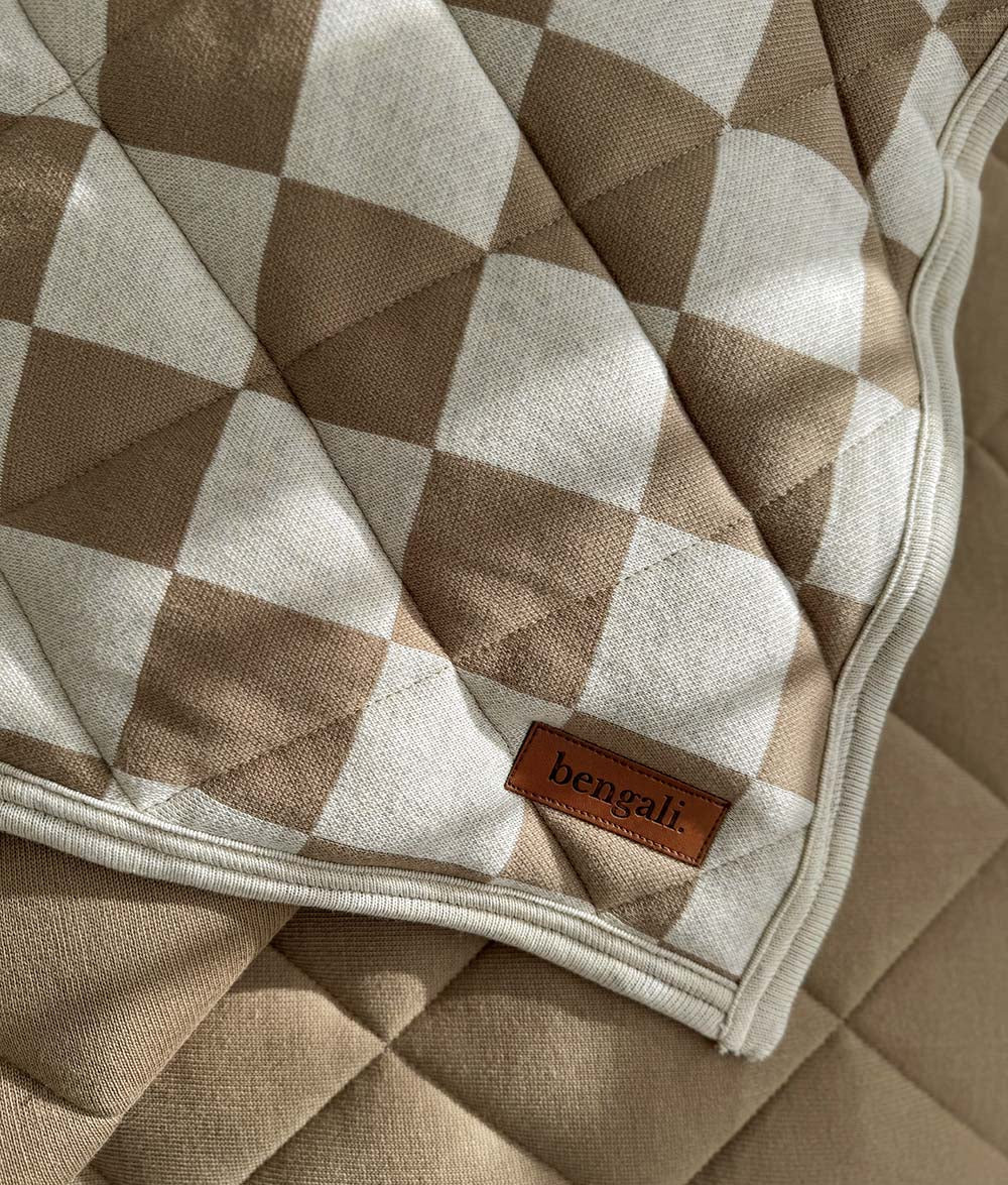 Corner of the khaki gingham quilt turned back to show the plain khaki reverse and Bengali tab