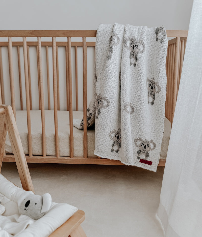 Nursery with a koala knit blanket over a timber cot rail and the Koala comforter in a bouncer