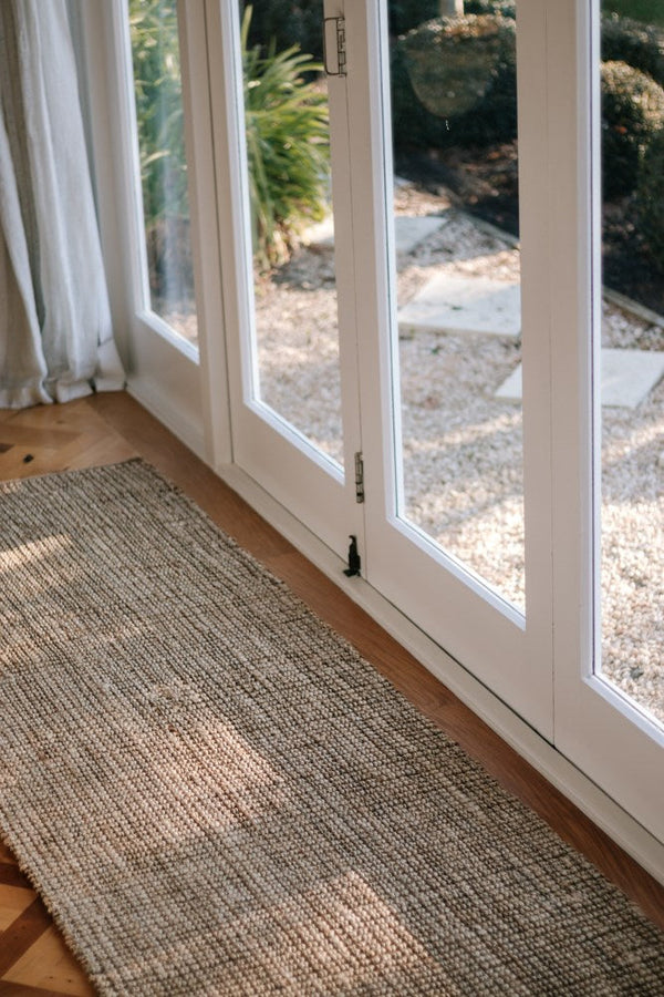 A Garcia Home Jute Runner Bubble Natural Brown 80x300cm rug in front of a sliding glass door, providing strength and durability.