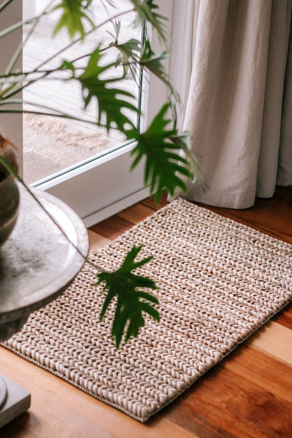 A Garcia Home Jute Mat Thick Tail Brown 60x90 made of jute fibers on a wooden floor next to a potted plant.