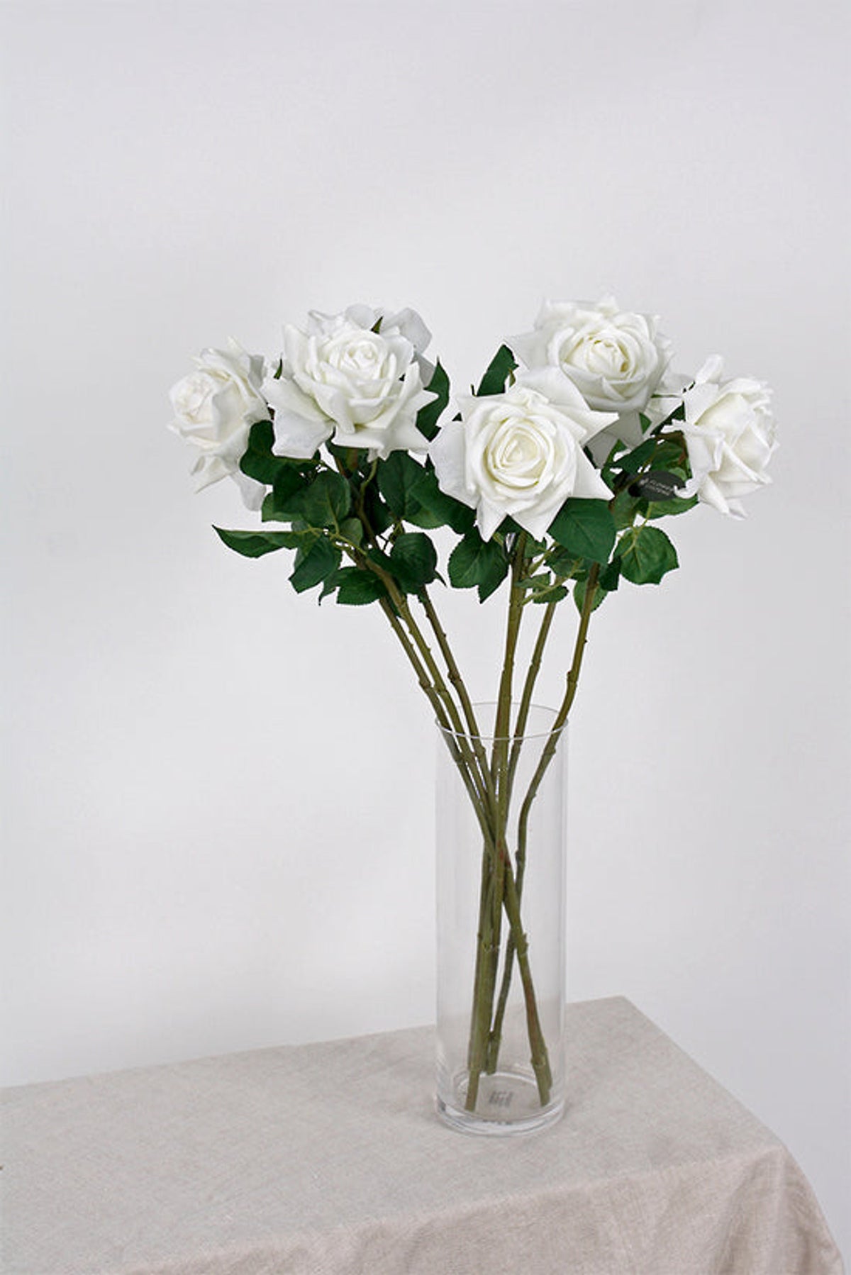 White roses in a tall clear glass vase on a draped side table