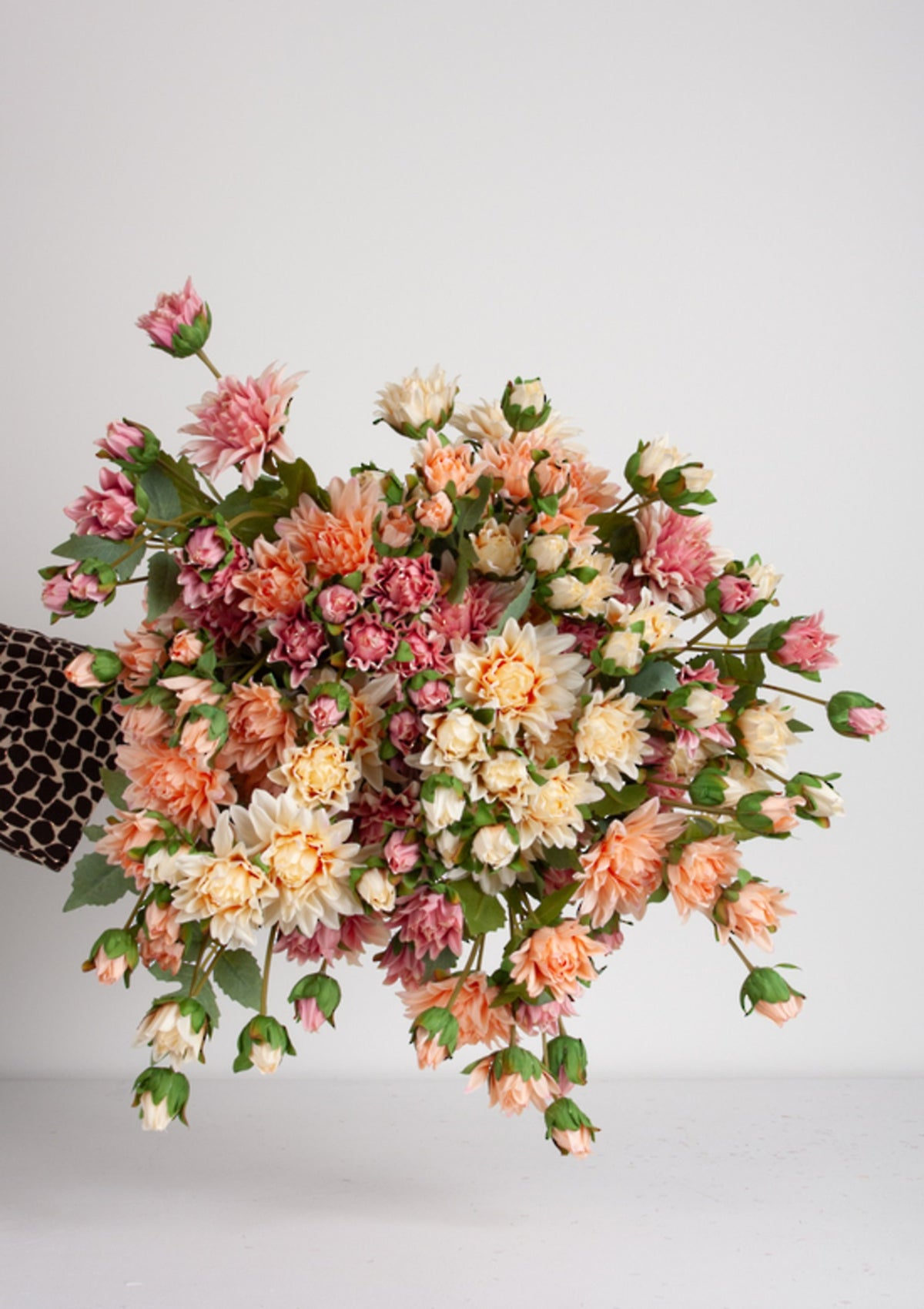 Large mixed bunch of pink, peach and cream mum sprays held out against grey