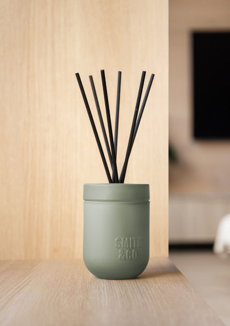 Smith and Co diffuser with black reeds on a pale timber surface against a timber wall