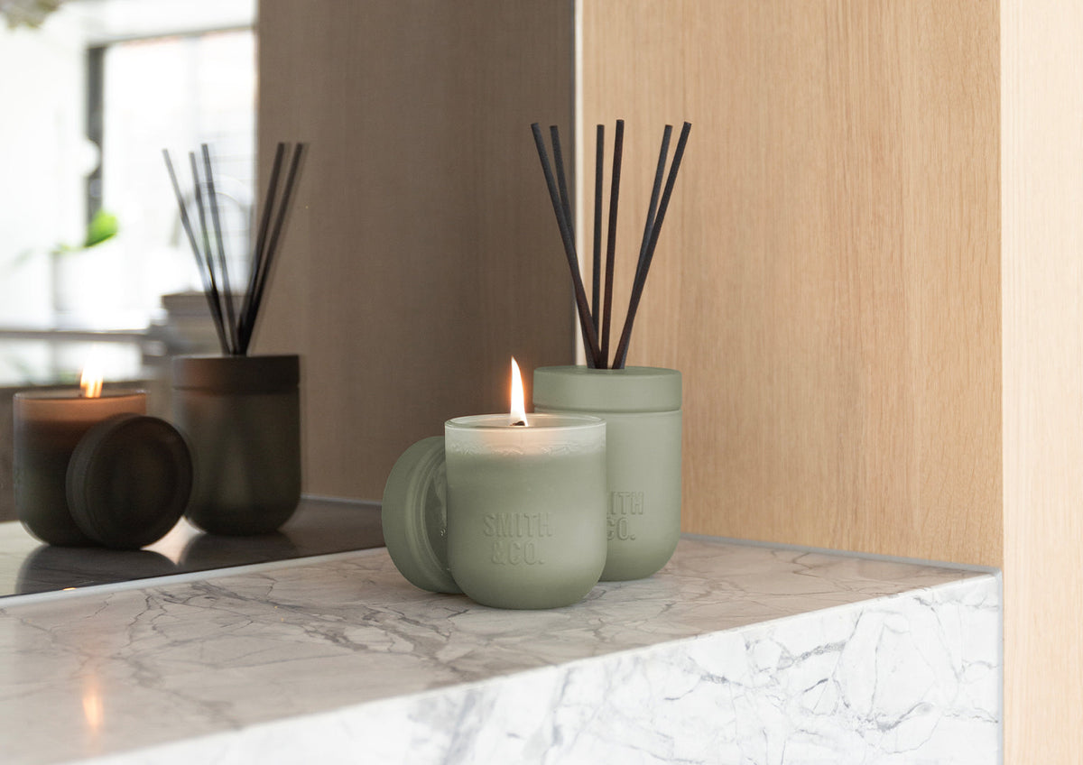 Lit sage green Smith and Co candle beside the reed diffuser on a marble ledge