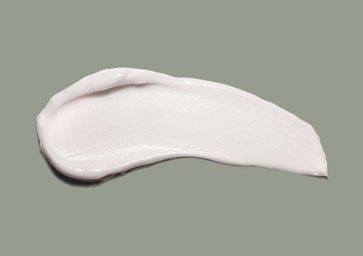 Swatch of white hand cream smeared across a sage green background