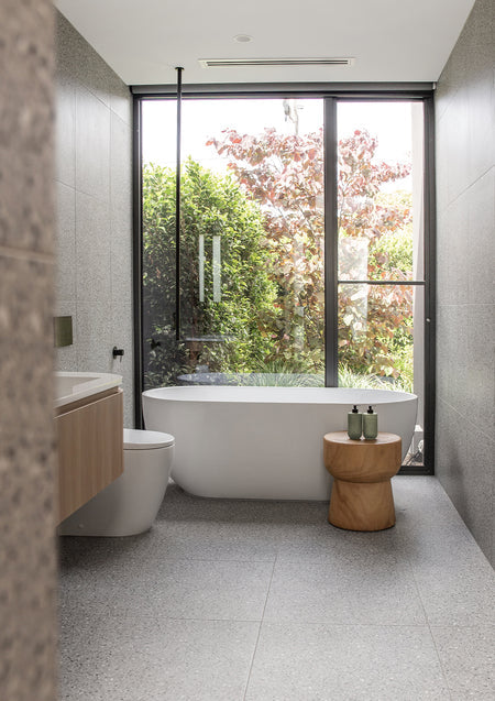 Bathroom with a freestanding bath under a garden window and a timber stool holding sage Smith & Co. bottles