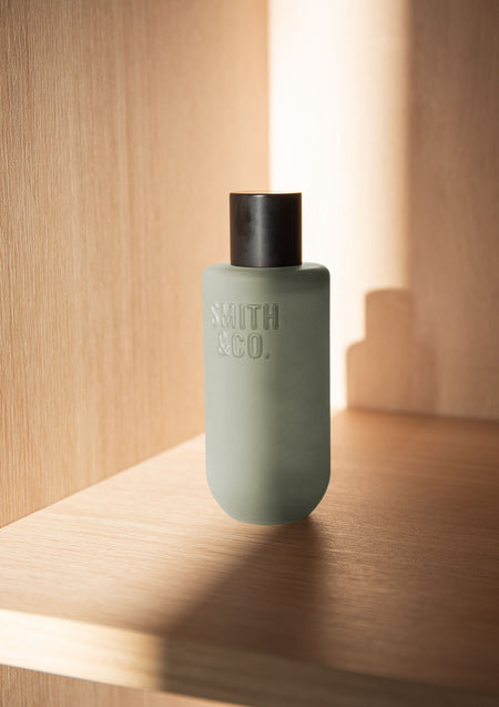 Sage green Smith & Co. room spray on an oak shelf in warm sunlight and shadow