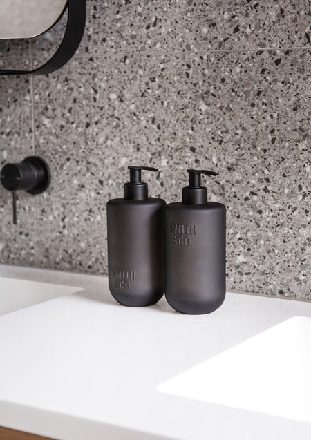 Two Smith & Co. pump bottles on a white vanity against a speckled terrazzo splashback