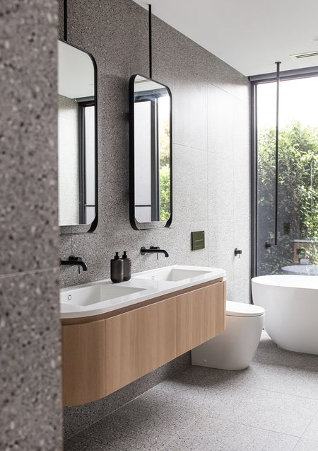 Terrazzo bathroom with a timber vanity, twin mirrors and a freestanding bath by the window