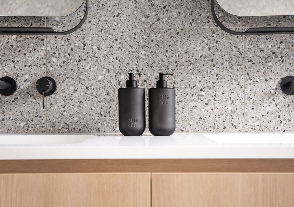 Two Smith & Co. bottles on a white basin top with black tapware and a timber vanity