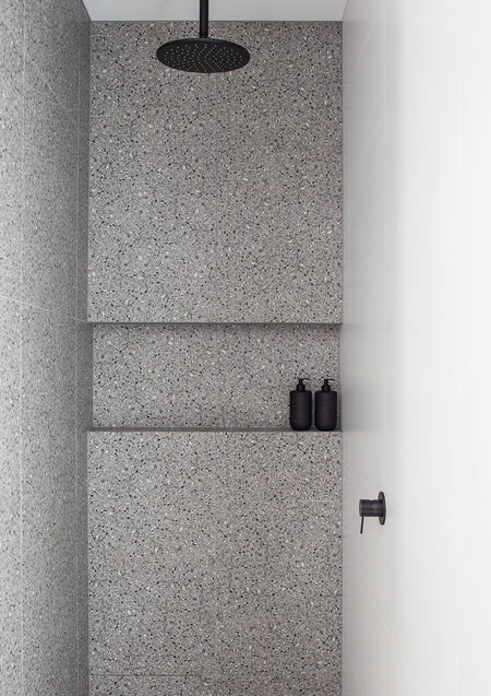 Terrazzo shower with a black rain head and Smith & Co. bottles on the ledge