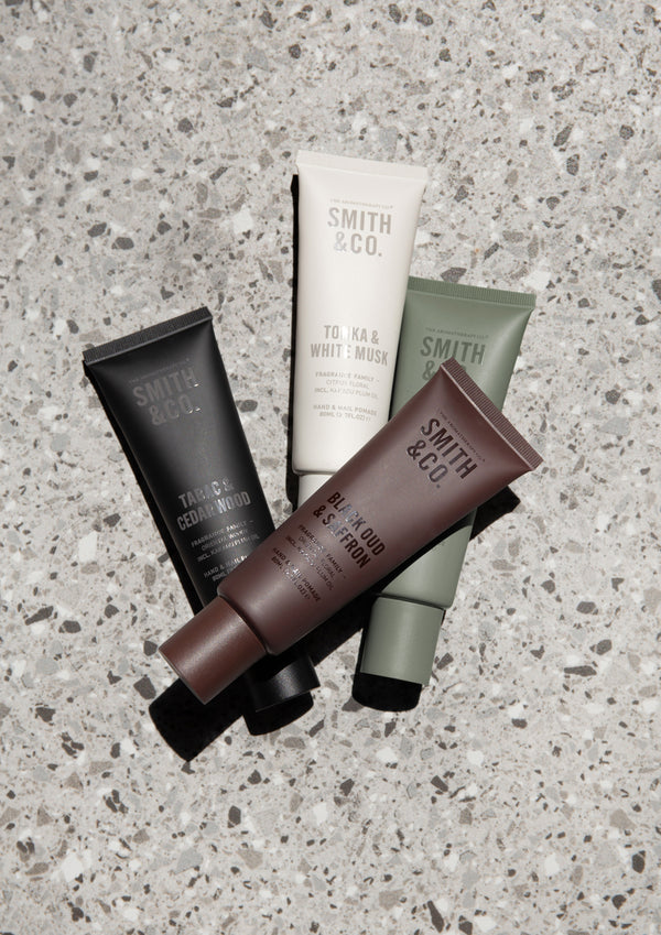 Four Smith and Co hand cream tubes in white, black, sage and brown arranged on grey terrazzo