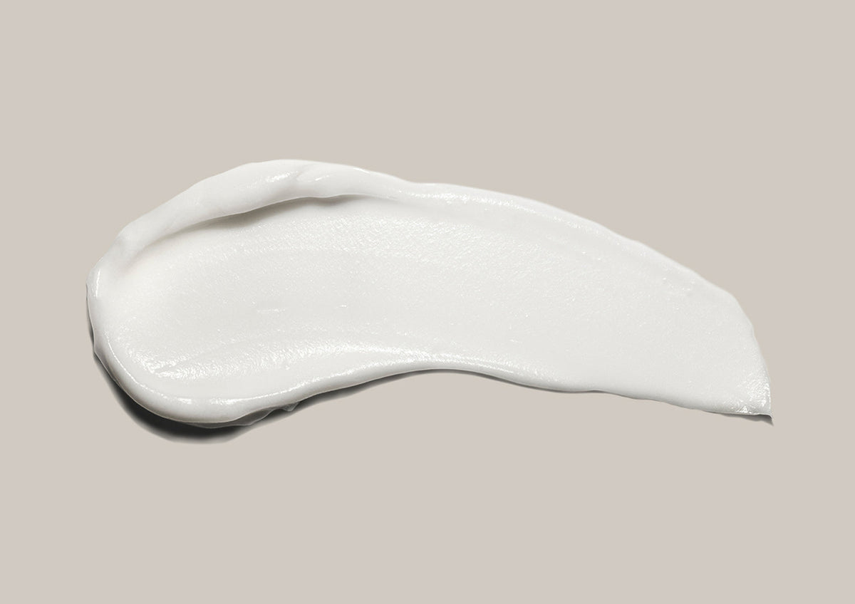 A swipe of white hand cream on a soft grey background