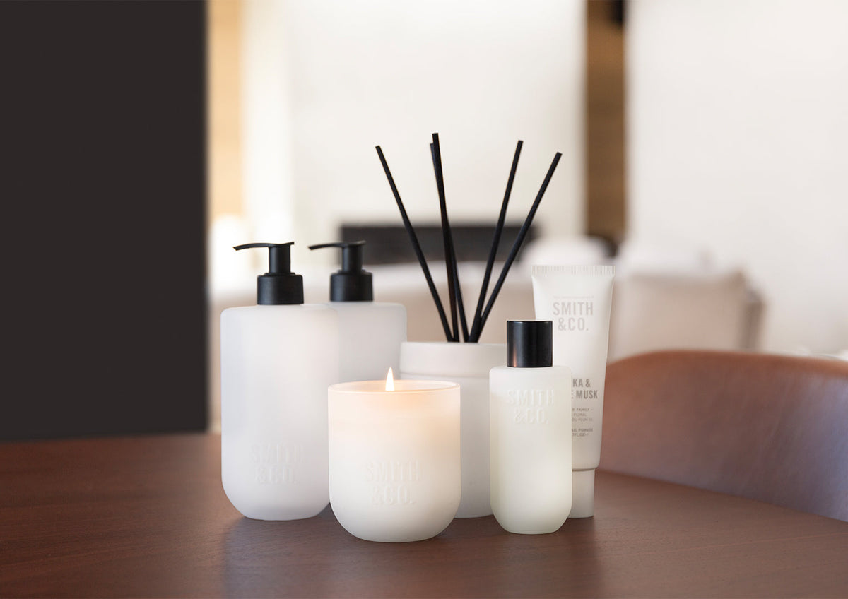 Smith and Co bottles with lit candles and a reed diffuser on a timber surface