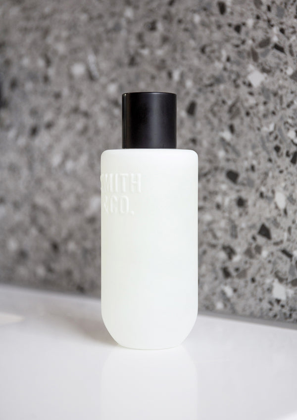 Close view of the frosted room spray bottle on a white ledge against speckled grey terrazzo