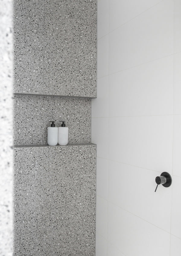 Two small Smith & Co. bottles in a terrazzo shower niche beside a white wall