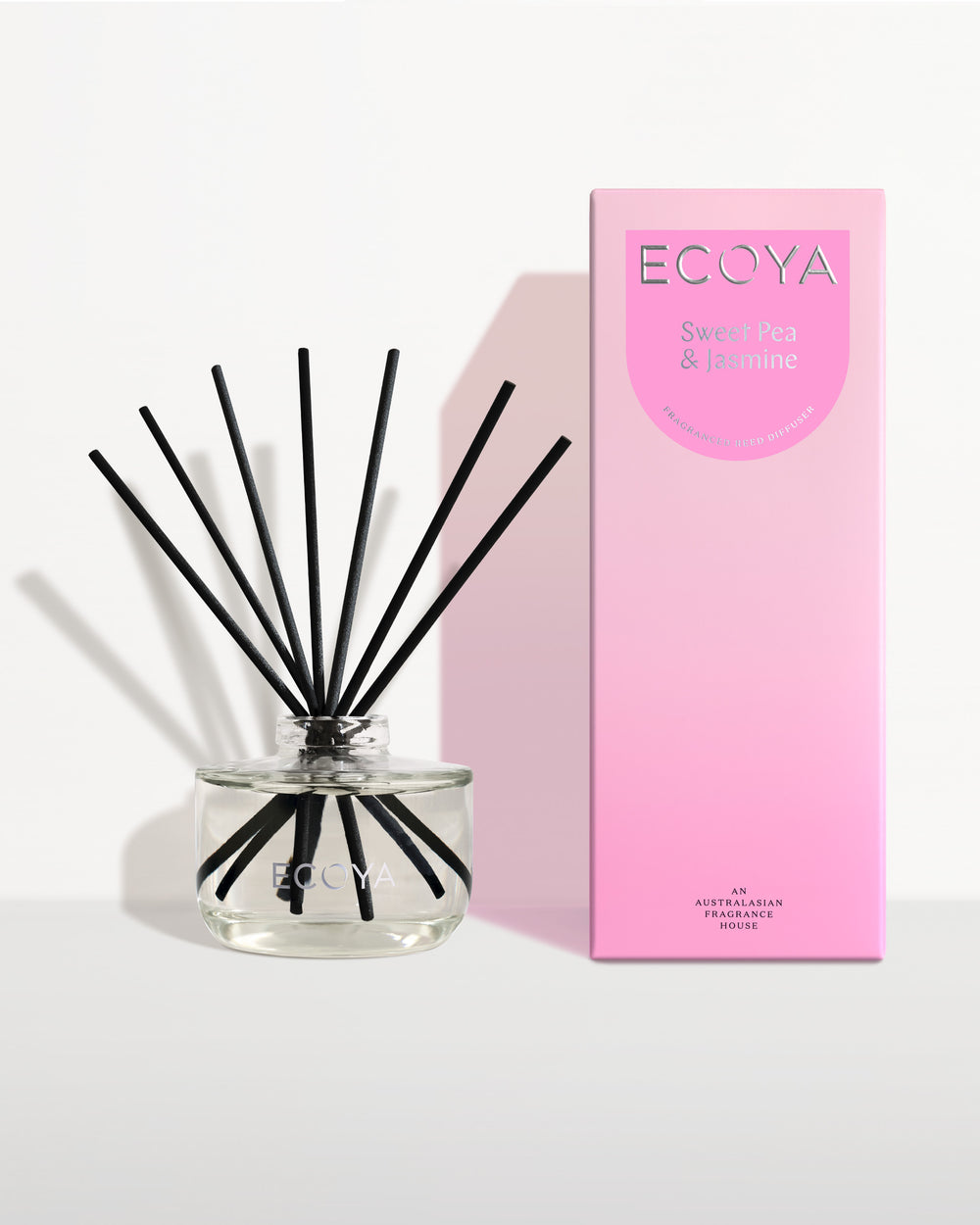 Ecoya Sweet Pea and Jasmine reed diffuser in a clear glass jar with black reeds, beside its pink gift box