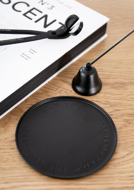 Black embossed plate with a candle snuffer and wick trimmer beside a white coffee table book