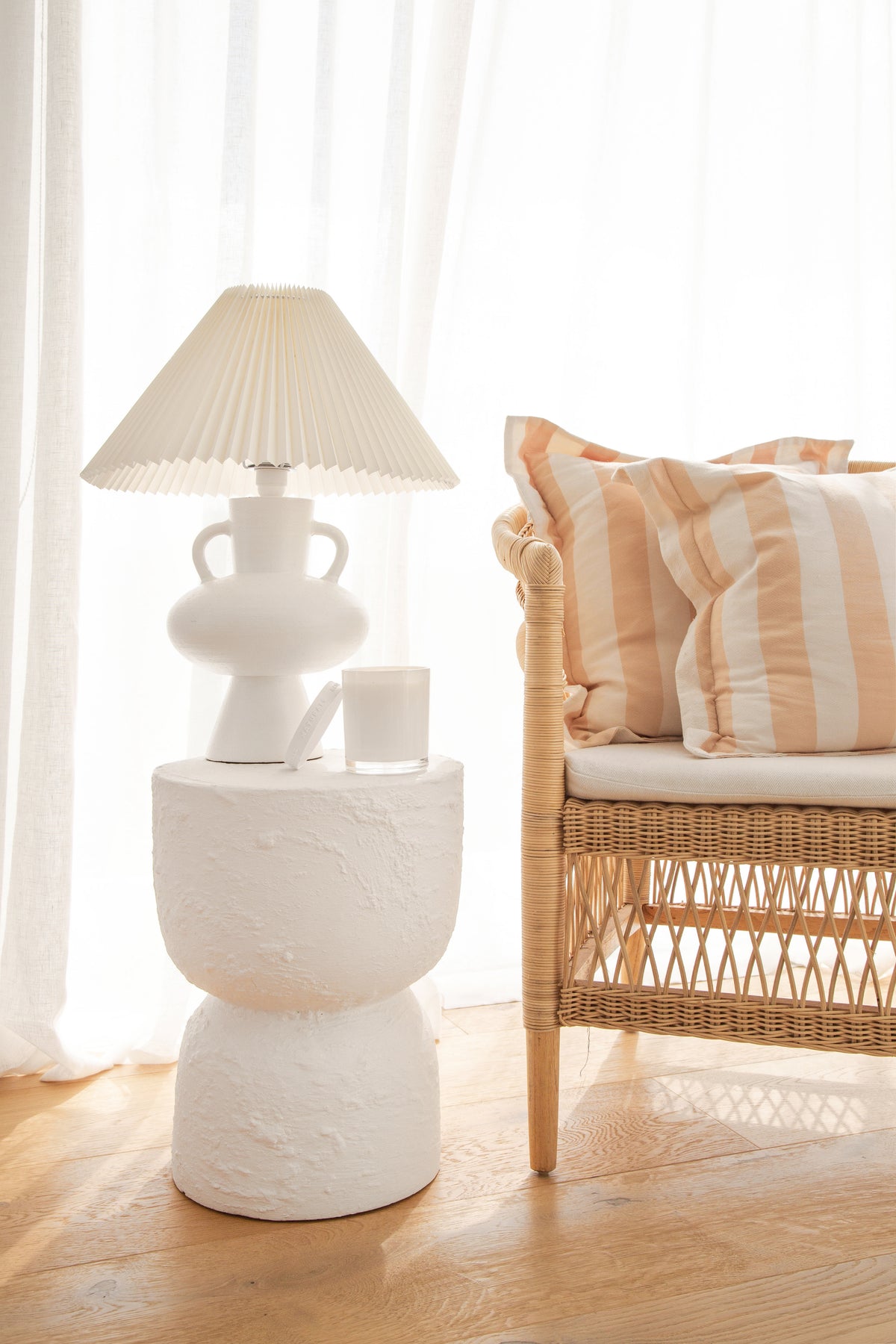 White sculptural lamp and the Naturals candle on a pedestal table beside a rattan chair