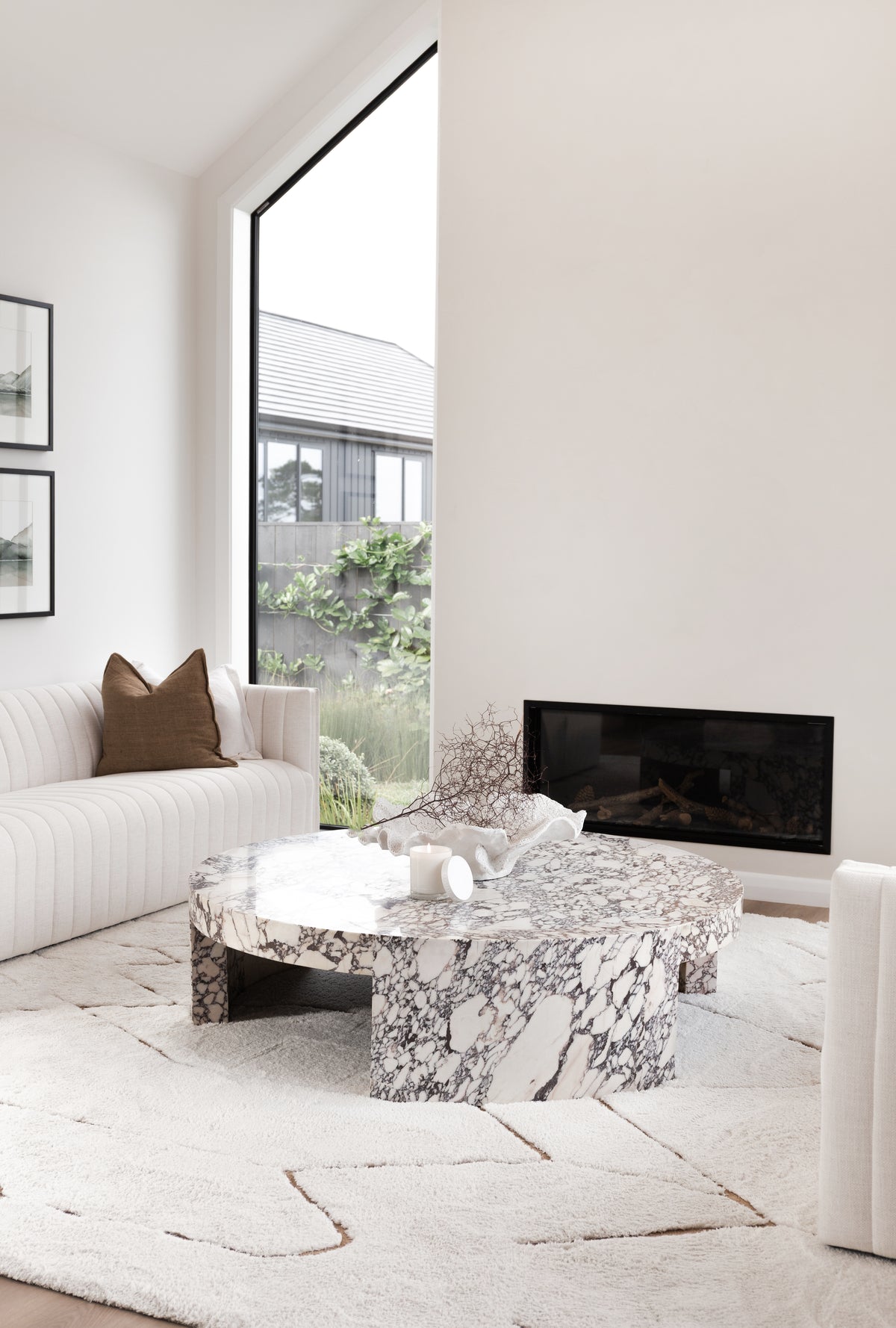 Pale living room with a fluted sofa, fireplace and a marble coffee table by tall windows