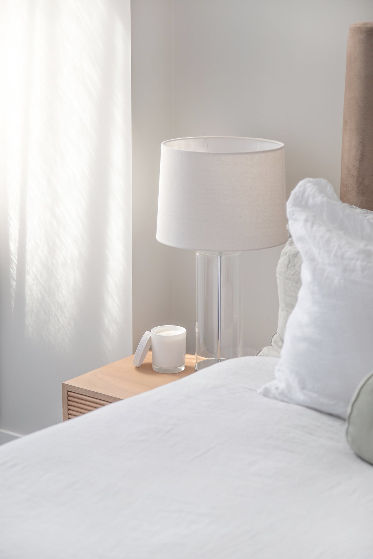 Naturals candle on a timber bedside table beside a lamp and white bedding