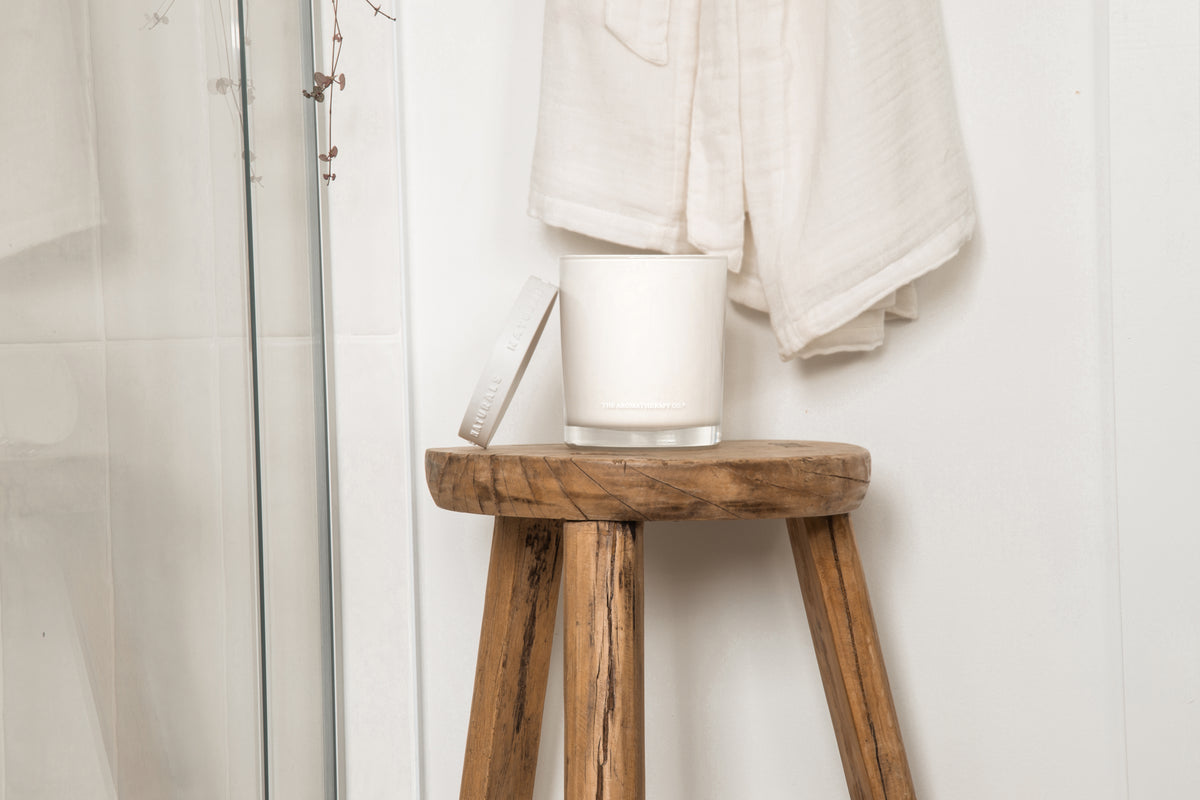 Naturals candle on a rustic timber stool in a bathroom with a folded white towel
