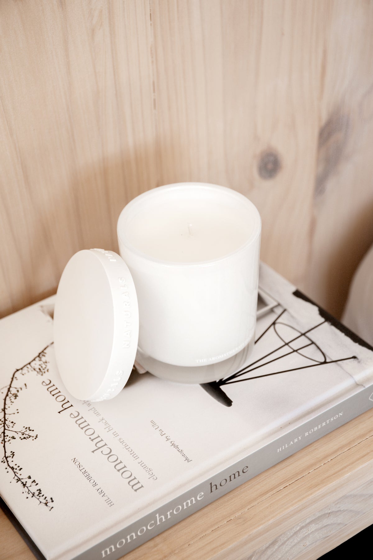 Naturals candle with its lid resting on a book against a pale timber wall