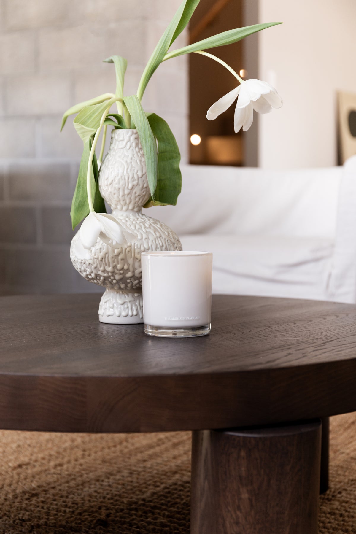 Naturals candle and a textured vase of tulips on a dark round table over a jute rug