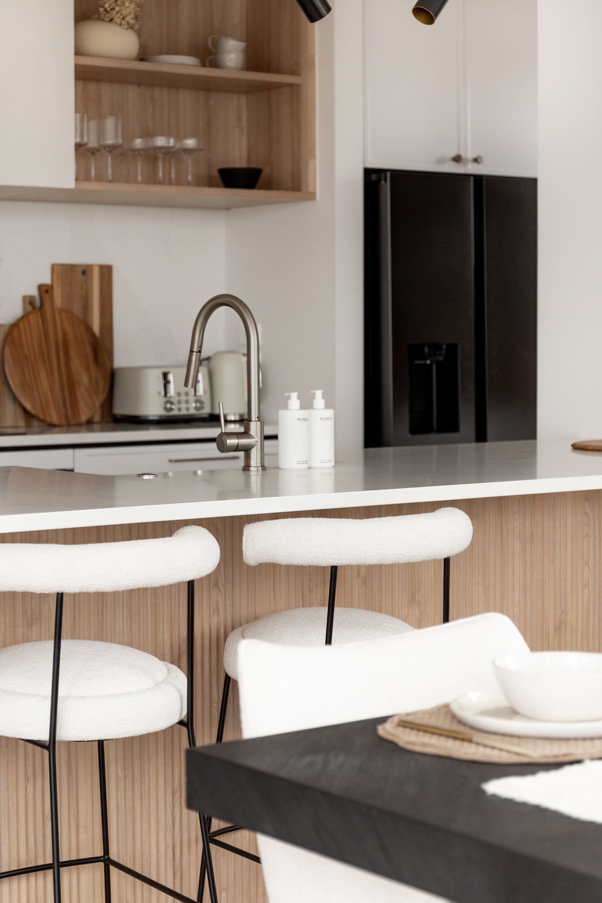 Kitchen bench with brushed tapware and two Naturals pump bottles, timber chopping boards against the splashback