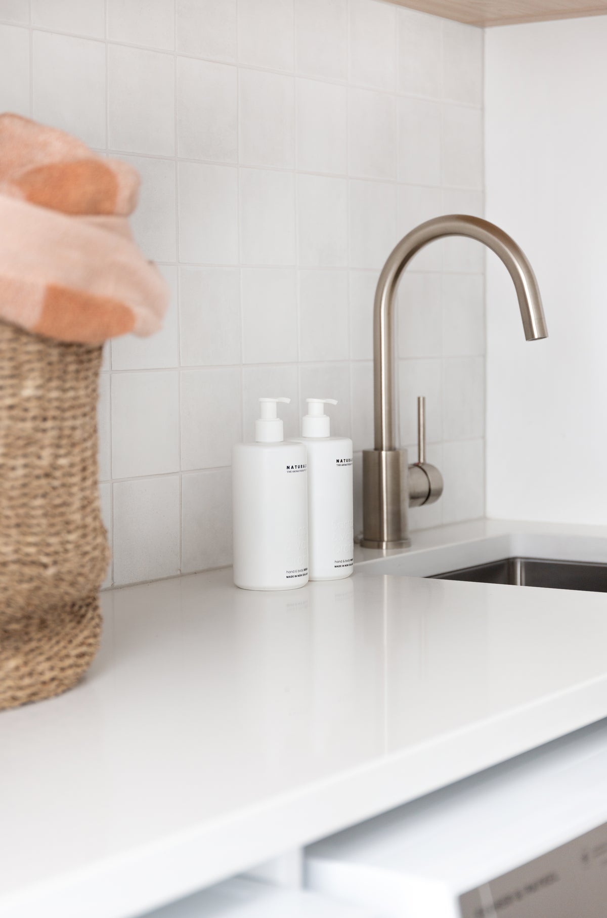 Laundry bench close up, brushed gooseneck tap, woven basket and a pair of white Naturals pump bottles