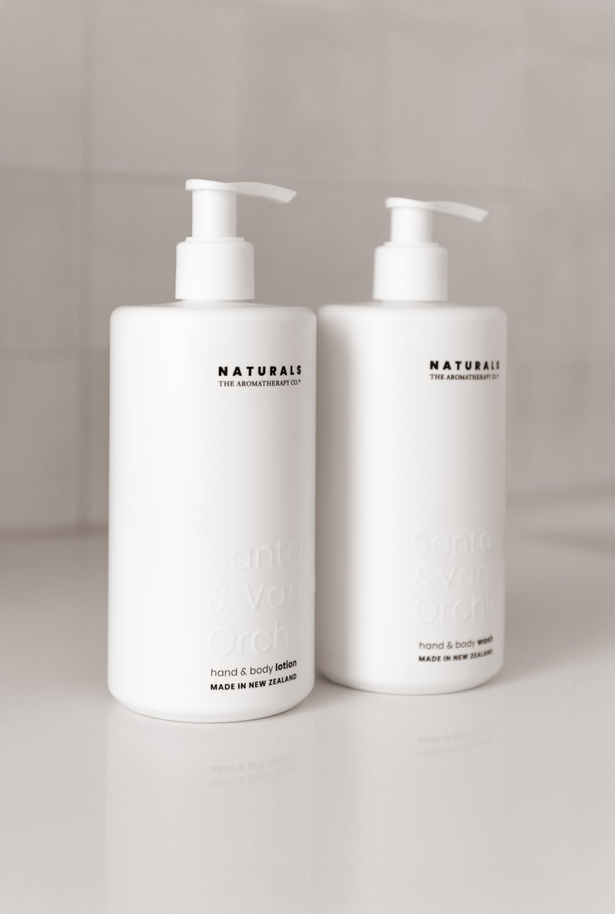 Close view of two frosted Naturals pump bottles, labels facing forward, tiled wall softly out of focus