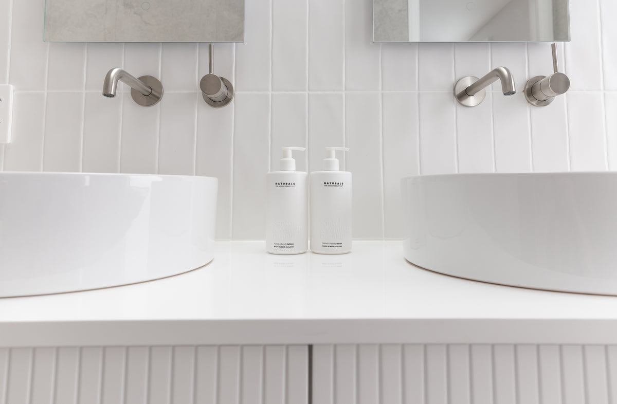 Wide double vanity with fluted cabinetry, round basins and a pair of Naturals bottles set between them