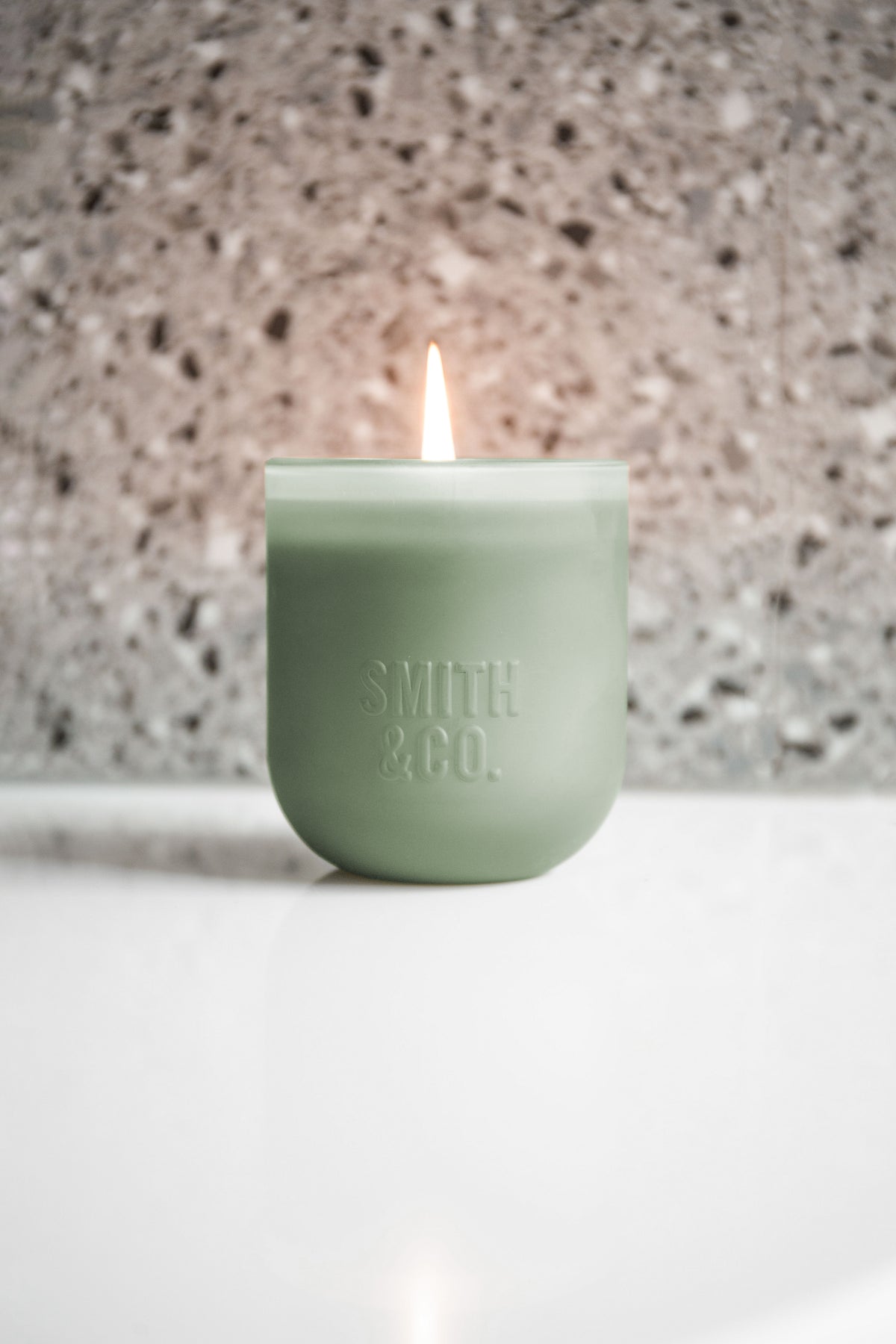 Lit Smith and Co candle on a white surface against a terrazzo wall