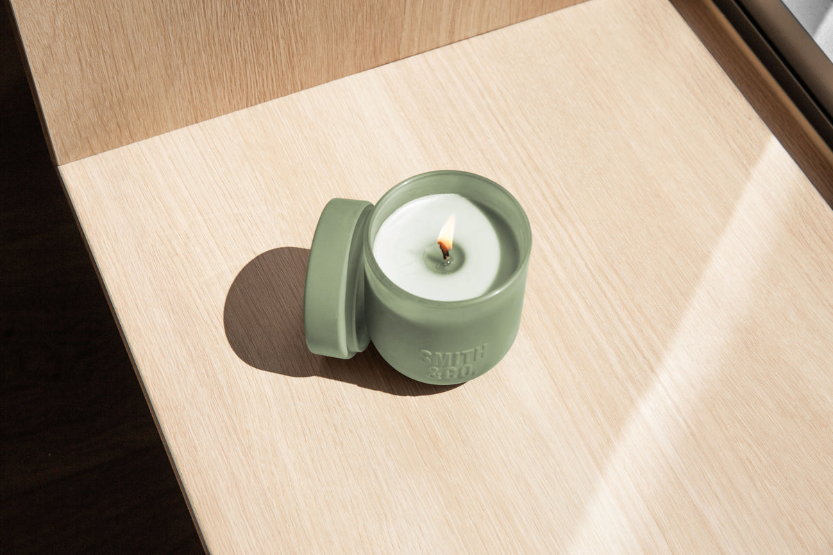 Lit Smith and Co candle with its lid beside it on a sunlit timber surface