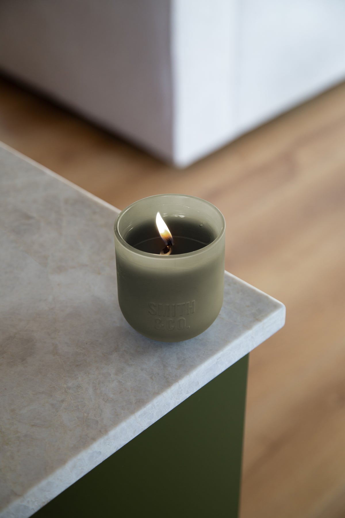 Lit Smith and Co candle on the corner of a stone bench above a timber floor