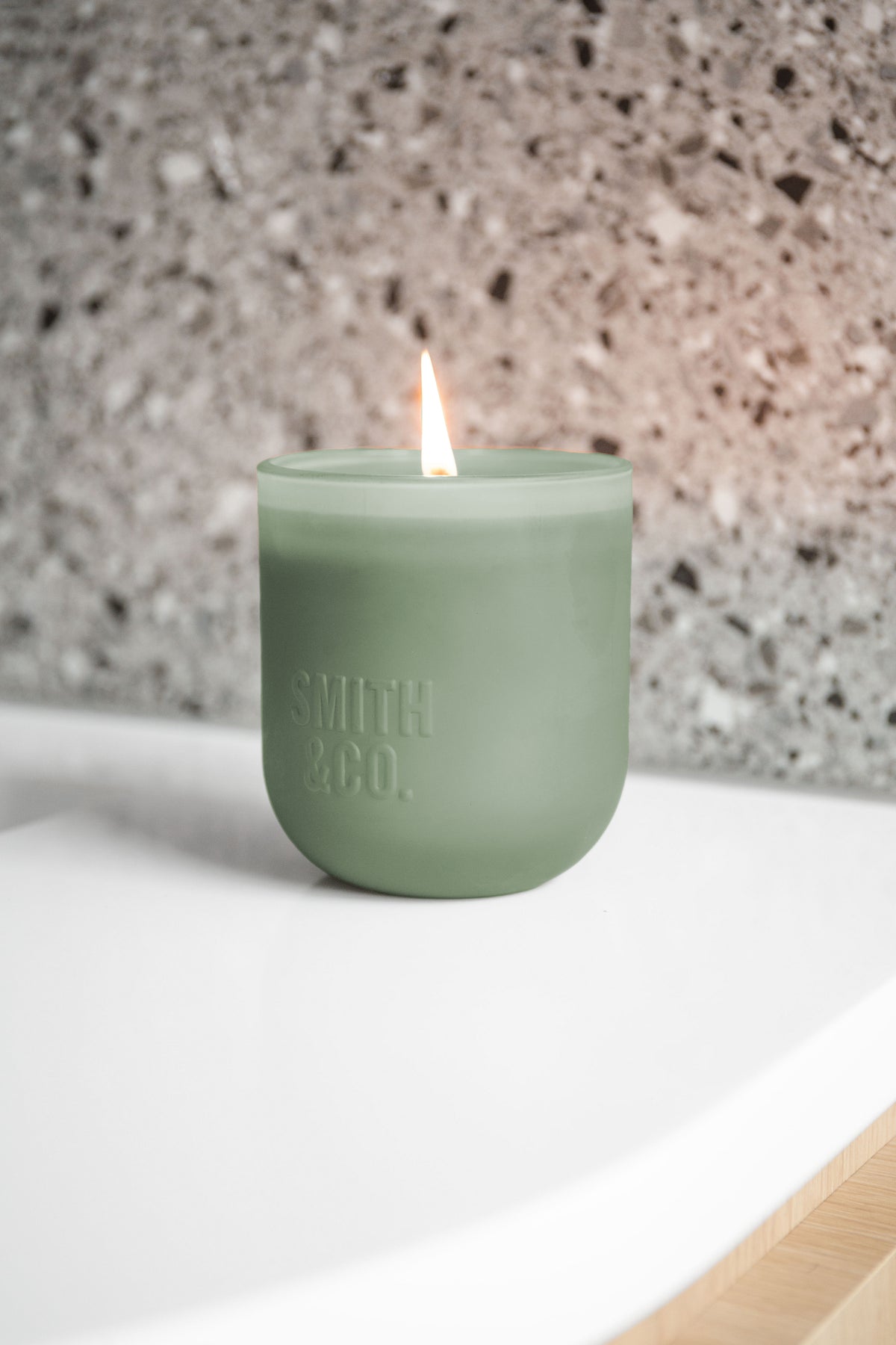 Lit Smith and Co candle on the edge of a white basin against terrazzo