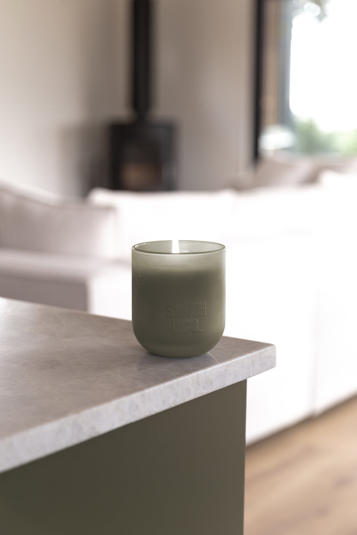 Lit Smith and Co candle on a stone kitchen island with a brass tap behind