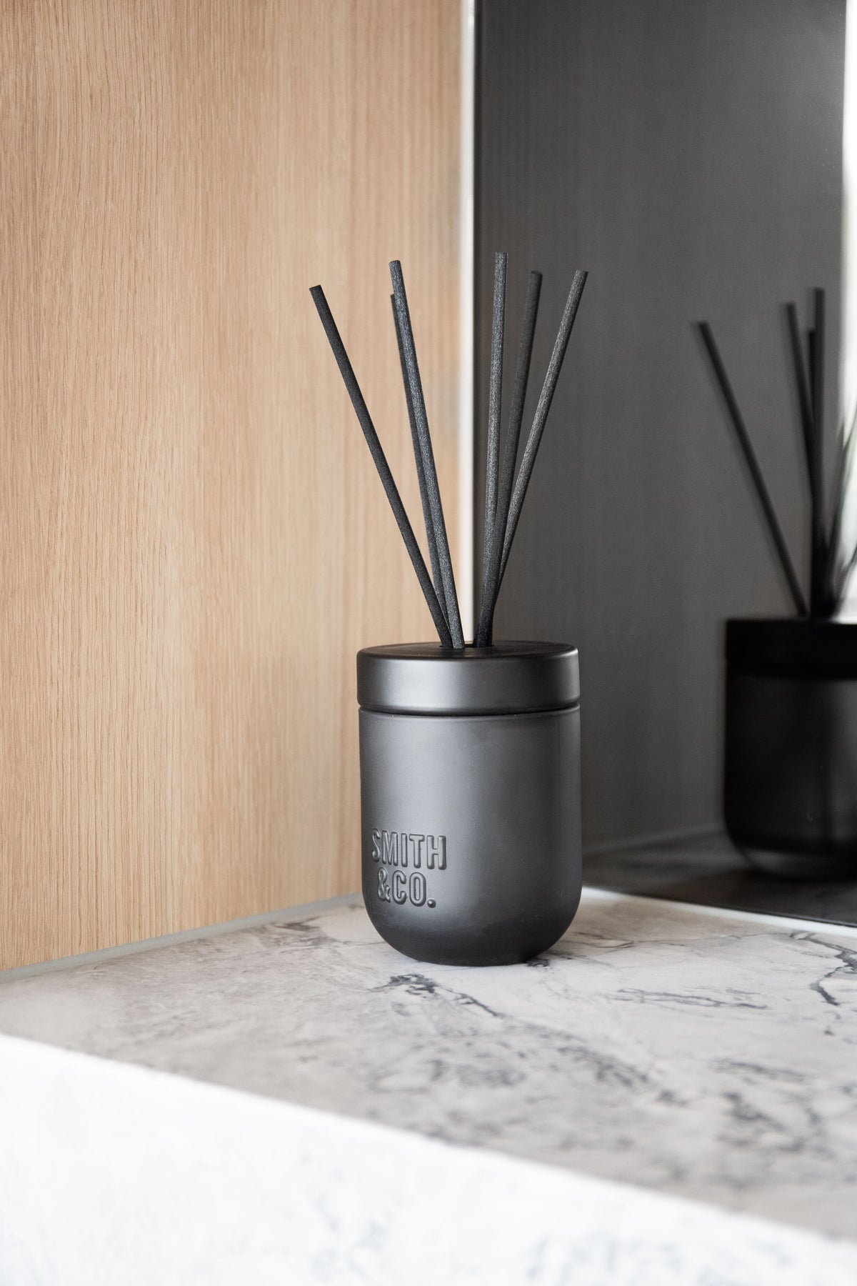 Two Smith & Co. diffusers on a marble ledge with timber panelling behind