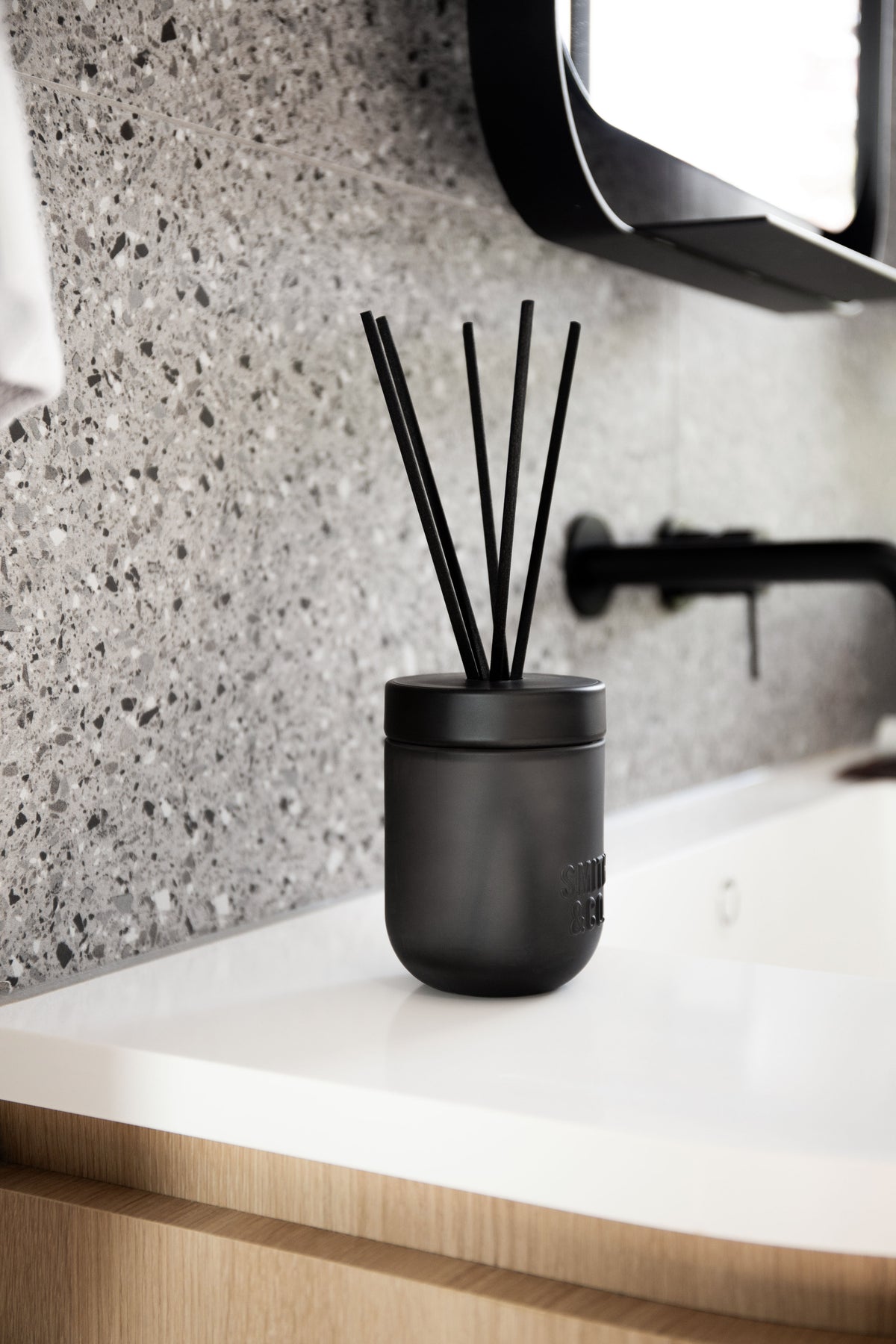 Smith & Co. diffuser on a white vanity with a black tap and mirror against terrazzo