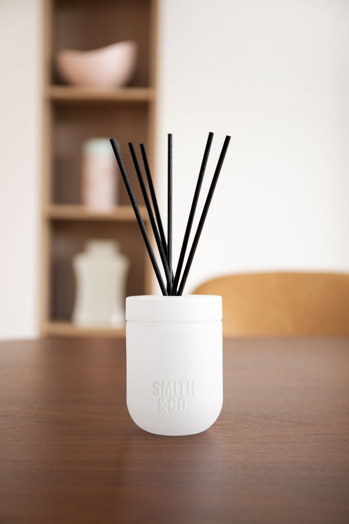 White Smith and Co diffuser on a dark timber table with blurred shelving behind