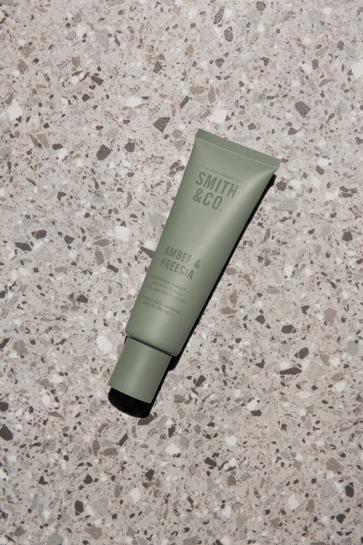 Sage green Smith & Co. tube lying on grey terrazzo, seen from above